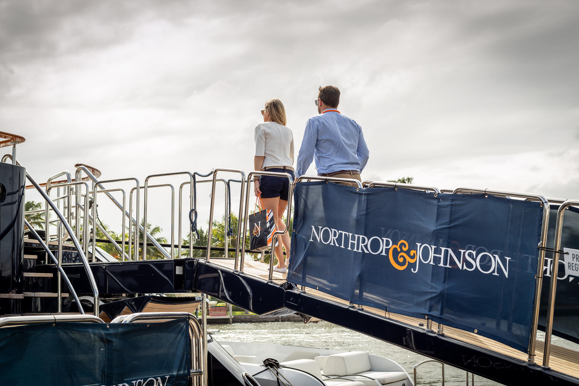 Man and woman boarding a superyacht with a Northrop & Johnson banner attached at the Fort Lauderdale International Boat Show